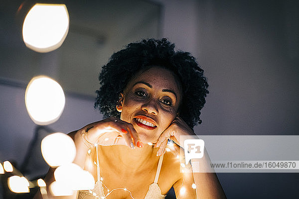 Nahaufnahme einer lächelnden Frau mit beleuchteter Lichterkette an einer Hauswand