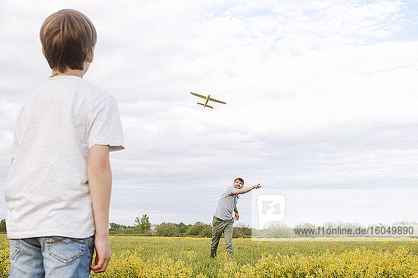 Vater und Sohn spielen mit Spielzeugflugzeug auf Rapsfeld gegen Himmel