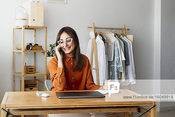 Weibliche Modedesignerin sitzt am Schreibtisch im Heimbüro und telefoniert
