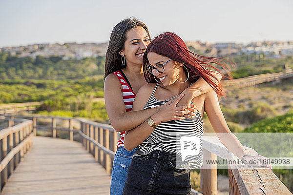 Fröhliche Teenager-Mädchen umarmen sich an der Strandpromenade gegen den klaren Himmel