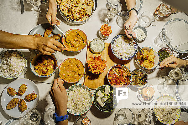 Hände von Menschen  die gemeinsam an einem mit indischen Speisen gedeckten Tisch essen