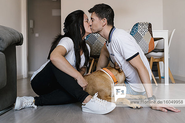 Paar  das sich küsst  während es neben dem Hund auf dem Fußboden zu Hause sitzt