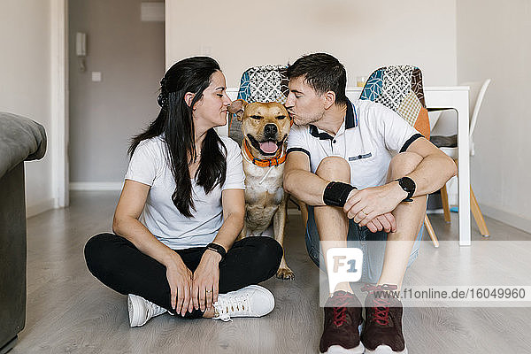 Couple kissing dog while sitting on floor at home