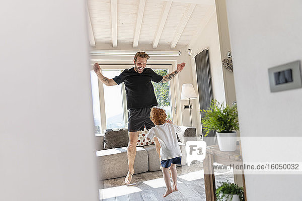 Fröhlicher Vater und Sohn springen beim Spielen im heimischen Wohnzimmer