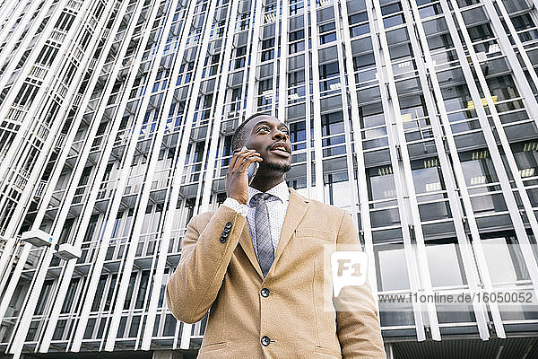 Junger Geschäftsmann vor einem modernen Bürogebäude in der Stadt beim Telefonieren