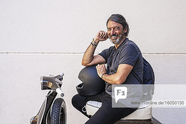 Happy man sitting on motor scooter against white wall