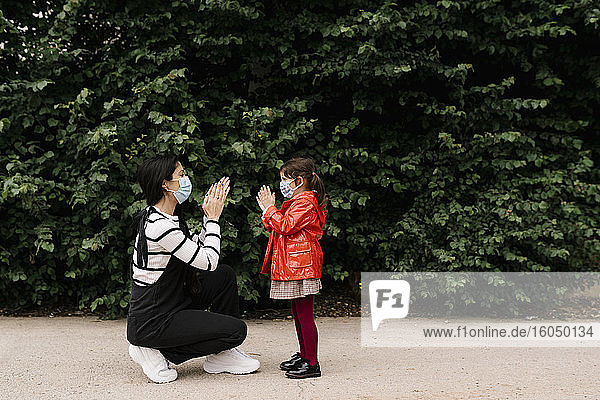 Mutter und Tochter tragen Masken und spielen auf der Straße ein Klatschspiel