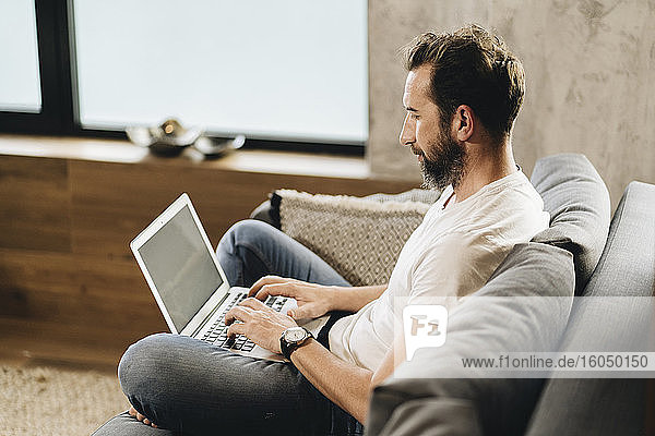 Mature man sitting on couch  using laptop