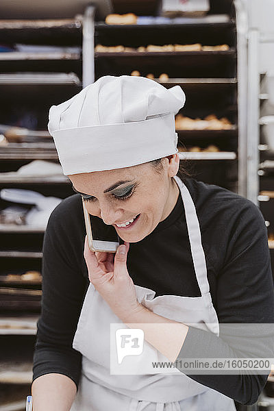 Glückliche Bäckerin benutzt Smartphone in Großküche