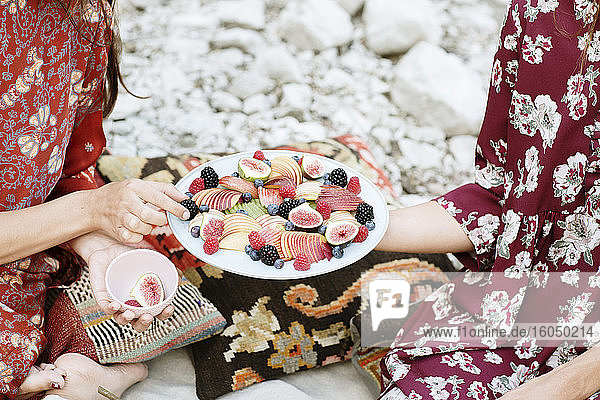 Nahaufnahme einer Frau  die einer Freundin beim Picknick Früchte anbietet