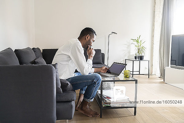 Mann sitzt auf der Couch in einer modernen Wohnung und benutzt einen Laptop