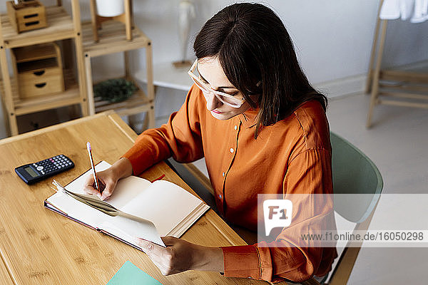 Female freelancer working at home sitting at desk using calculator