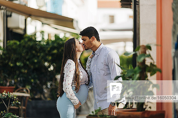 Romantisches schwangeres Paar küsst sich in der Stadt an einem sonnigen Tag