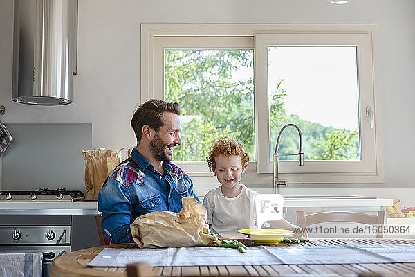 Glücklicher Vater und Sohn  die am Esstisch mit grünen Erbsen in der Küche sitzen und genießen