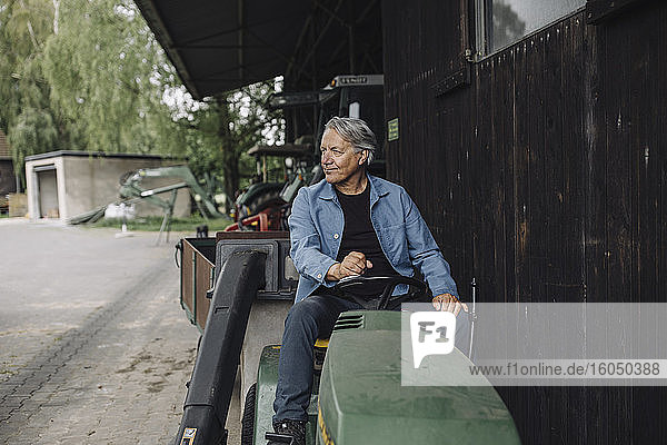 Älterer Mann fährt Traktor mit Anhänger auf einem Bauernhof