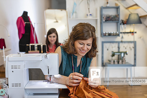 Eine lächelnde Schneiderin betrachtet einen Stoff an einer Nähmaschine in einem Designstudio