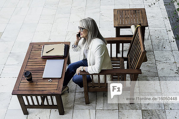Weibliche Fachkraft sitzt auf einem Stuhl und spricht mit einem Mobiltelefon im Garten