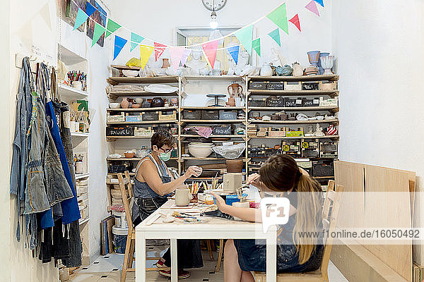 Frauen mit Masken arbeiten an einer Werkbank im Atelier
