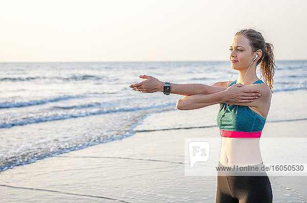 Sportliche Frau  die sich bei Sonnenaufgang am Meer reckt  Gran Canaria  Spanien