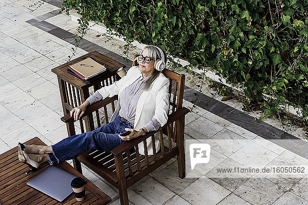 Ältere weibliche Fachkraft hört Musik und entspannt sich auf einem Stuhl im Garten