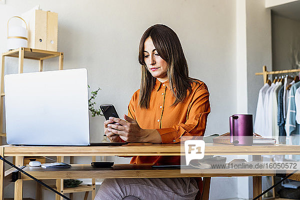 Modedesignerin arbeitet zu Hause am Schreibtisch mit Smartphone und Laptop