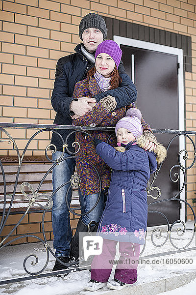 Nettes Mädchen mit Eltern vor dem Haus im Winter stehend
