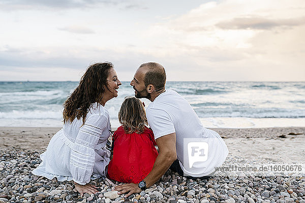 Couple about to kissing while sitting with daughter on shore at beach