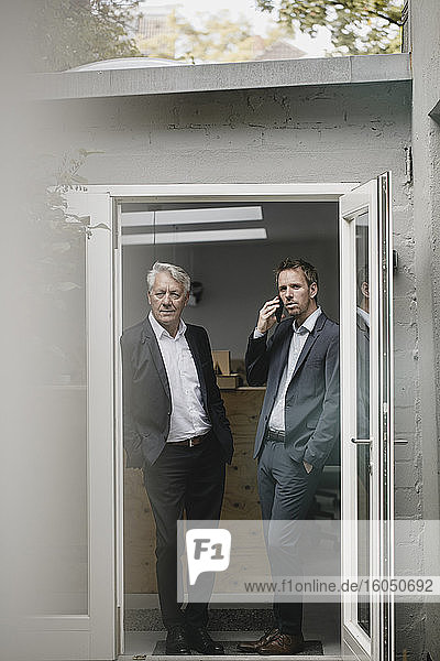 Two businessmen staning in open office door  talking on the phone