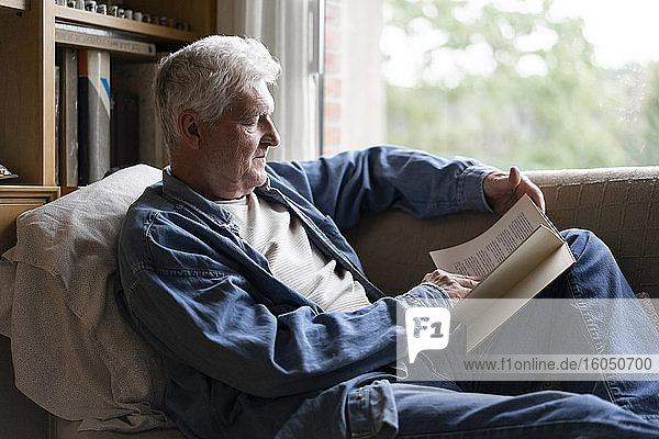 Senior man reading book while relaxing on sofa at home