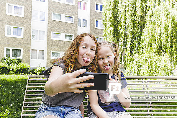 Schwestern machen Selfie mit herausgestreckten Zungen im Park