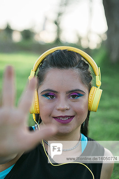 Teenager-Mädchen mit Down-Syndrom trägt 8s buntes Make-up und hört Musik mit gelben Kopfhörern