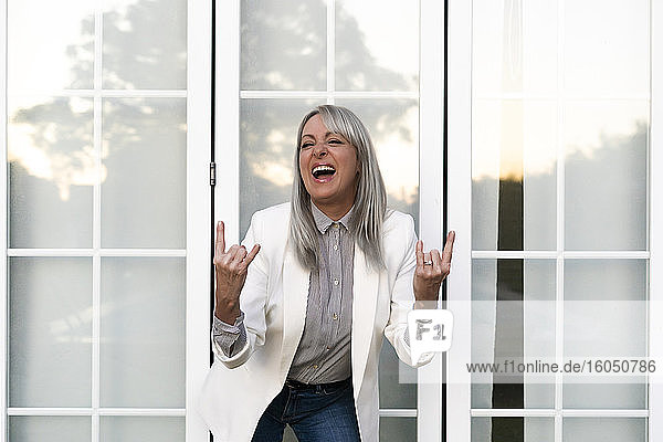 Fröhliche ältere Geschäftsfrau zeigt ein Hupenzeichen  während sie vor der Bürotür steht