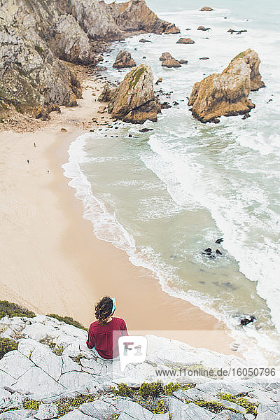 Junge Frau schaut auf das Meer  während sie auf einem Berg sitzt  Strand Ursa  Portugal