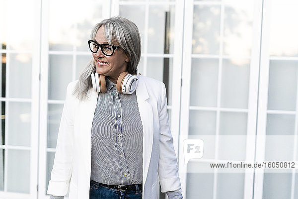 Smiling female professional looking away with headphones around neck