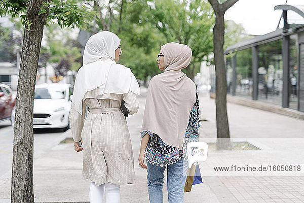 Muslim sisters talking while walking on sidewalk in city