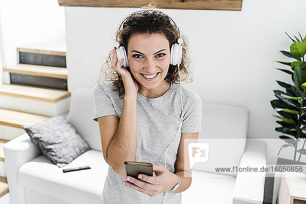 Porträt einer lächelnden jungen Frau  die mit Kopfhörern und Mobiltelefon Musik hört