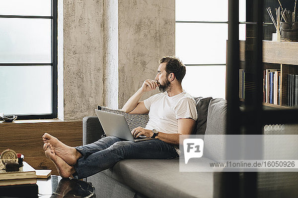 Mature man sitting on couch  using laptop  thinking