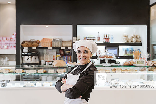 Confident female baker standing arms crossed at bakery