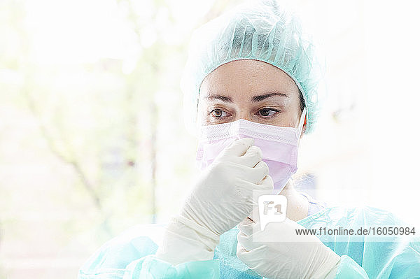 Nahaufnahme einer Krankenschwester mit chirurgischer Maske vor einem Fenster im Krankenhaus