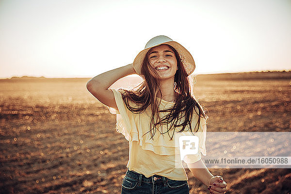 Fröhliche junge Frau steht bei Sonnenuntergang auf einem Feld