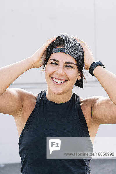 Close-up of smiling young woman wearing cap while standing against wall