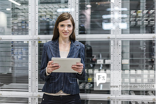 Lächelnde Geschäftsfrau  die ein digitales Tablet benutzt  während sie in einer Fabrik vor Glas steht