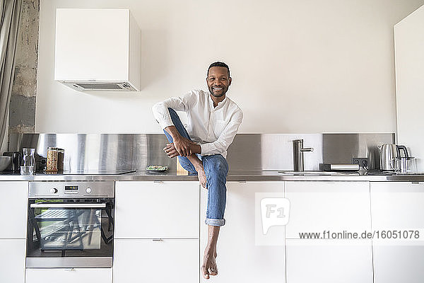 Porträt eines lächelnden Mannes  der zu Hause barfuß auf dem Küchentisch sitzt