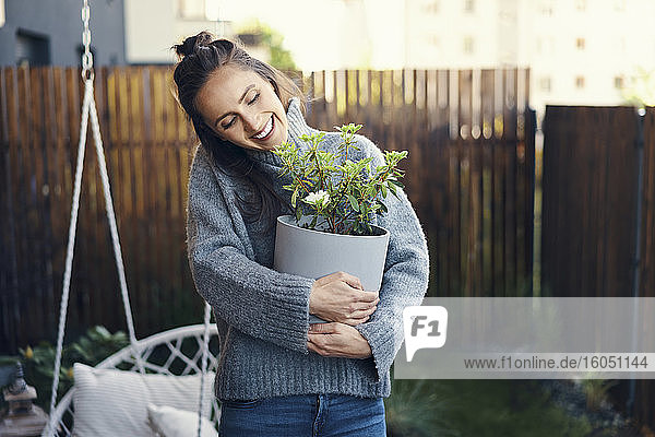 Fröhliche Frau  die eine Topfpflanze trägt  während sie im Hof steht