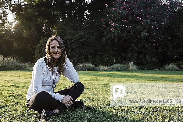 Glückliche erwachsene Frau sitzt im Gras im Park