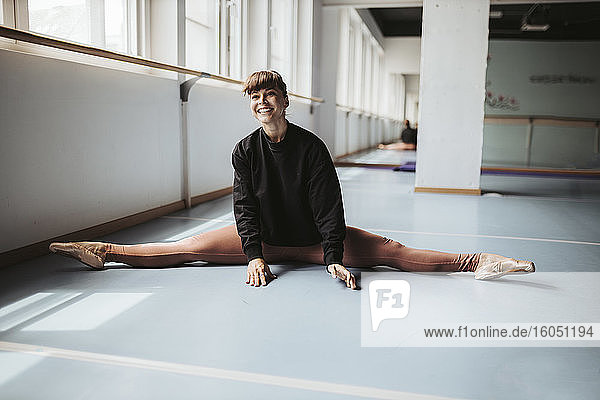 Glückliche Balletttänzerin streckt die Beine auf dem Boden im Tanzstudio