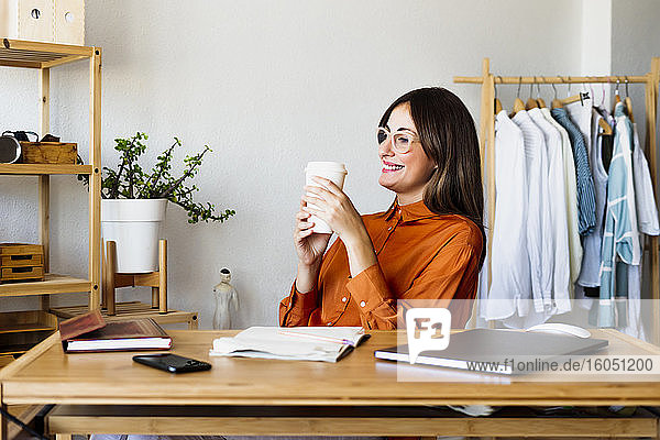 Weibliche Modedesignerin sitzt zu Hause am Schreibtisch und macht eine Kaffeepause