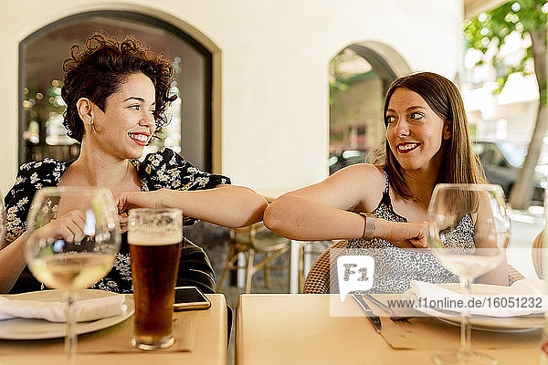 Lächelnde schöne junge Frauen grüßen mit Ellbogenstoß beim Sitzen im Restaurant