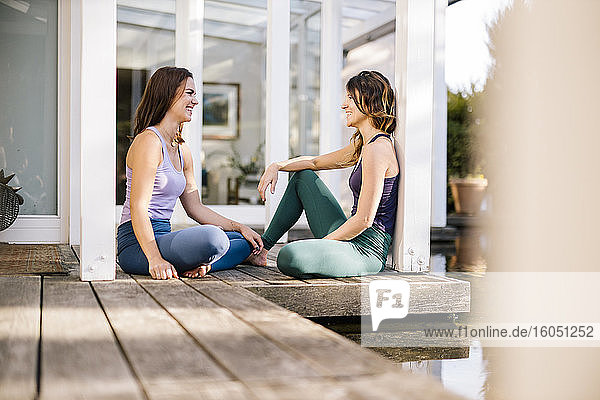 Weibliche Freunde unterhalten sich  während sie an Säulen auf dem Hartholzboden sitzen