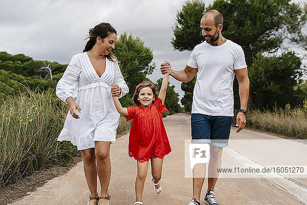 Glückliches Mädchen  das mit seinen Eltern auf einer Landstraße spazieren geht
